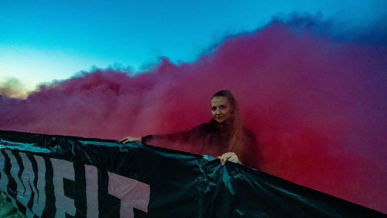 Eine junge Frau hält ein Transparent in den Händen und steht dabei in einem roten Nebel