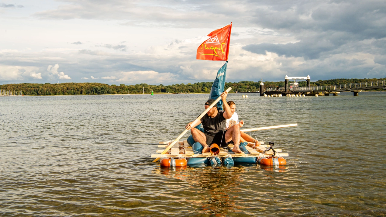Zwei Junge Leute mit einem selbst gebauten Floss auf dem Wasser