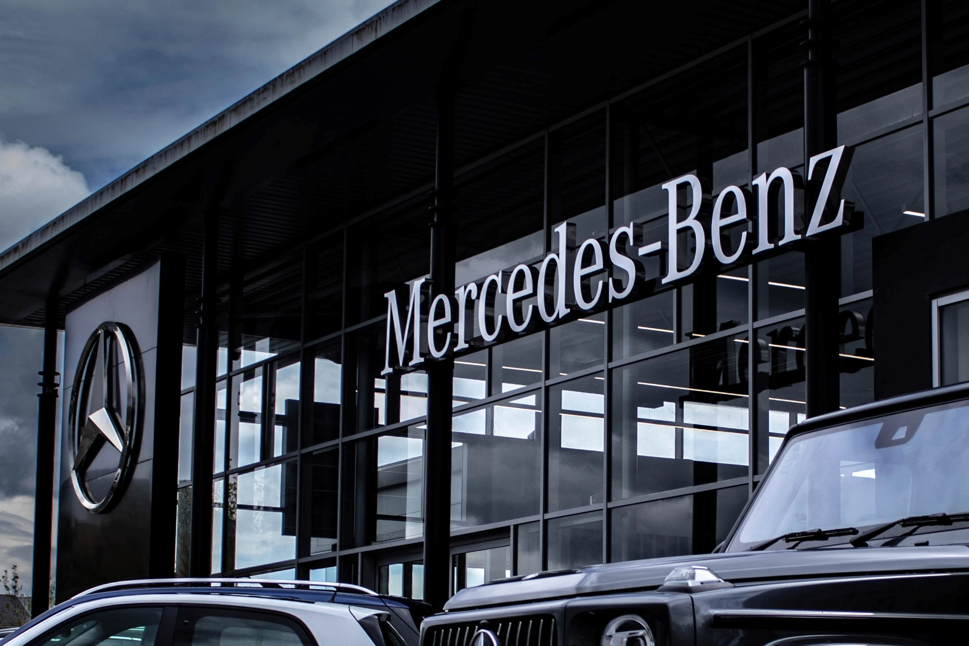 Es Steht ein Mercedes-Benz Geländewagen vor einem gläsernen Gebäude das ebenfalls den Schriftzug Mercedes-Benz trägt. 