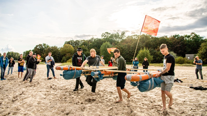 Eine Gruppe junger Leuten bringen das gebaute Floss zum Wasser