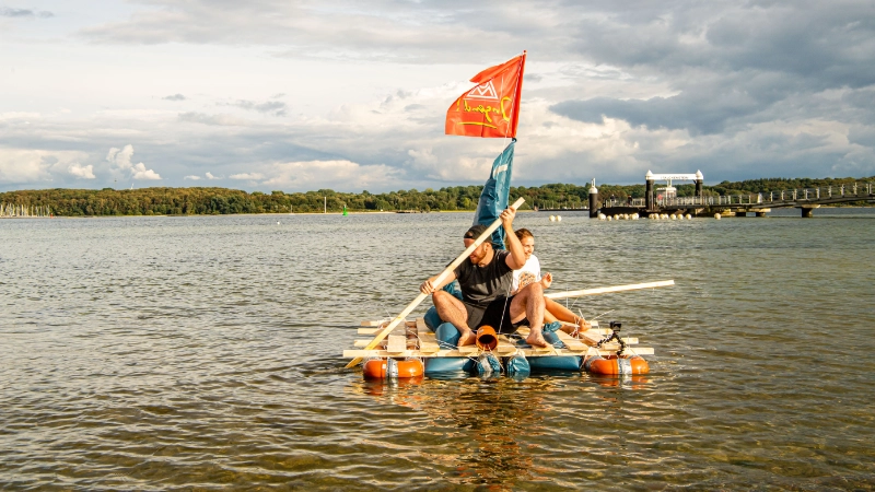 Zwei Junge Leute mit einem selbst gebauten Floss auf dem Wasser