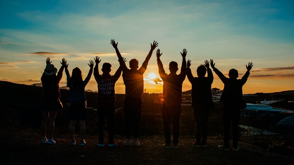 Eine Gruppe junger Leute stehen vor dem Sonnenuntergang und heben die Hände hoch